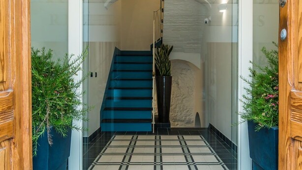 A modern entrance with a glass door, a blue staircase, and potted plants. - Cafe Bleu Relais (Sassari)