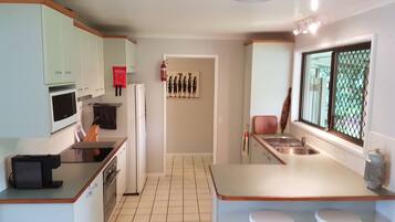 A modern kitchen with white cabinets, a microwave, a refrigerator, and a sink. There is a fire extinguisher on the wall and a window with a view of greenery.