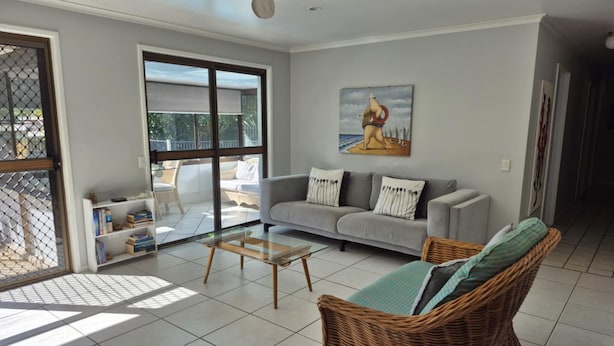 A living room with a sofa, a wicker chair, a coffee table, and a bookshelf. - Beerwah House, 3Bedroom , swimming pool, near Australia Zoo, Sunshine Coast (Beerwah)
