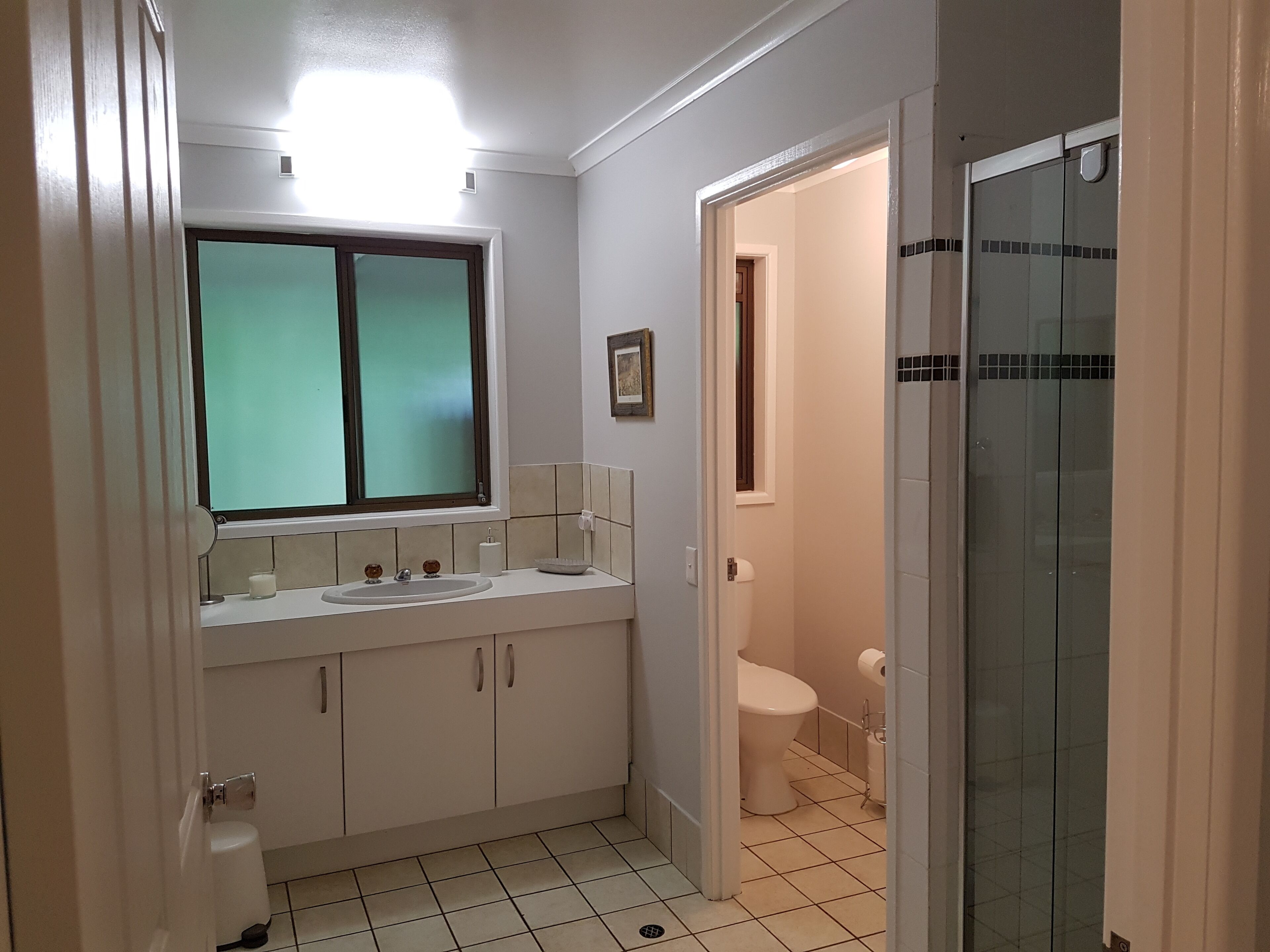 A bathroom with a double sink, toilet, and a glass shower enclosure.