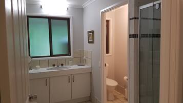 A bathroom with a double sink, toilet, and a glass shower enclosure.