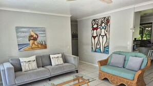 A living room with a grey sofa, a wicker sofa, a glass coffee table, and two wall art pieces. - Beerwah House, 3Bedroom , swimming pool, near Australia Zoo, Sunshine Coast (Beerwah)