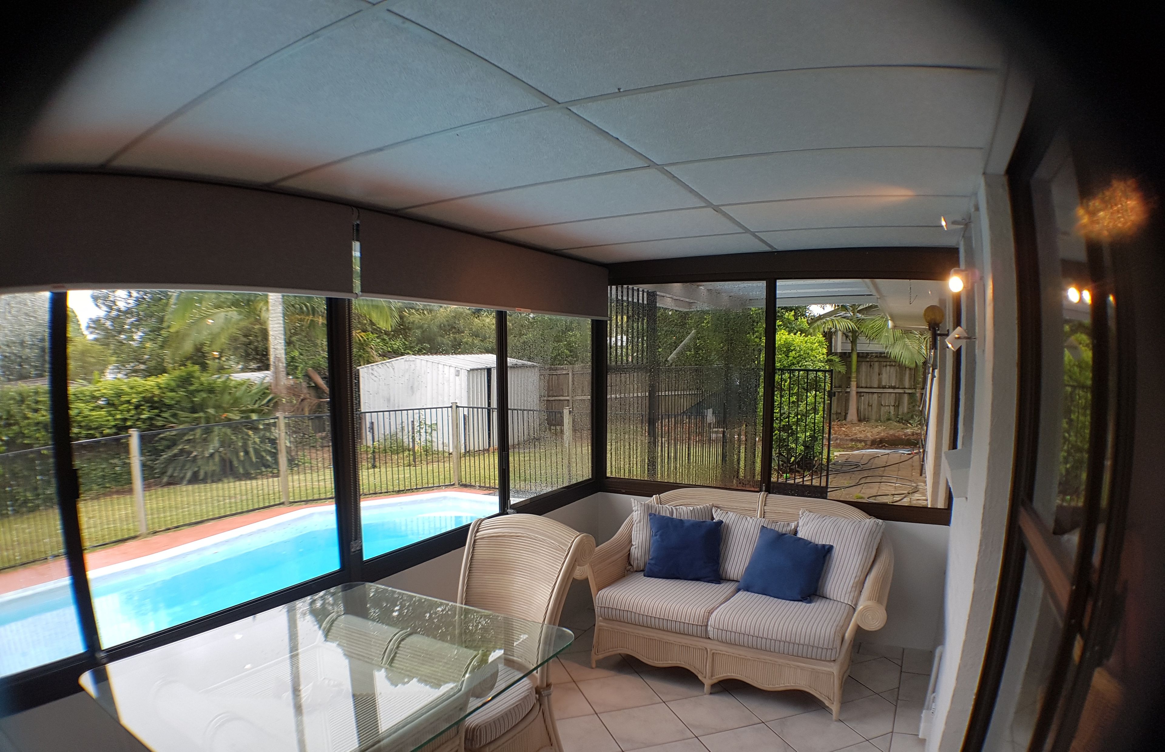 A sunroom with a glass table, wicker sofa, and a view of a backyard swimming pool.