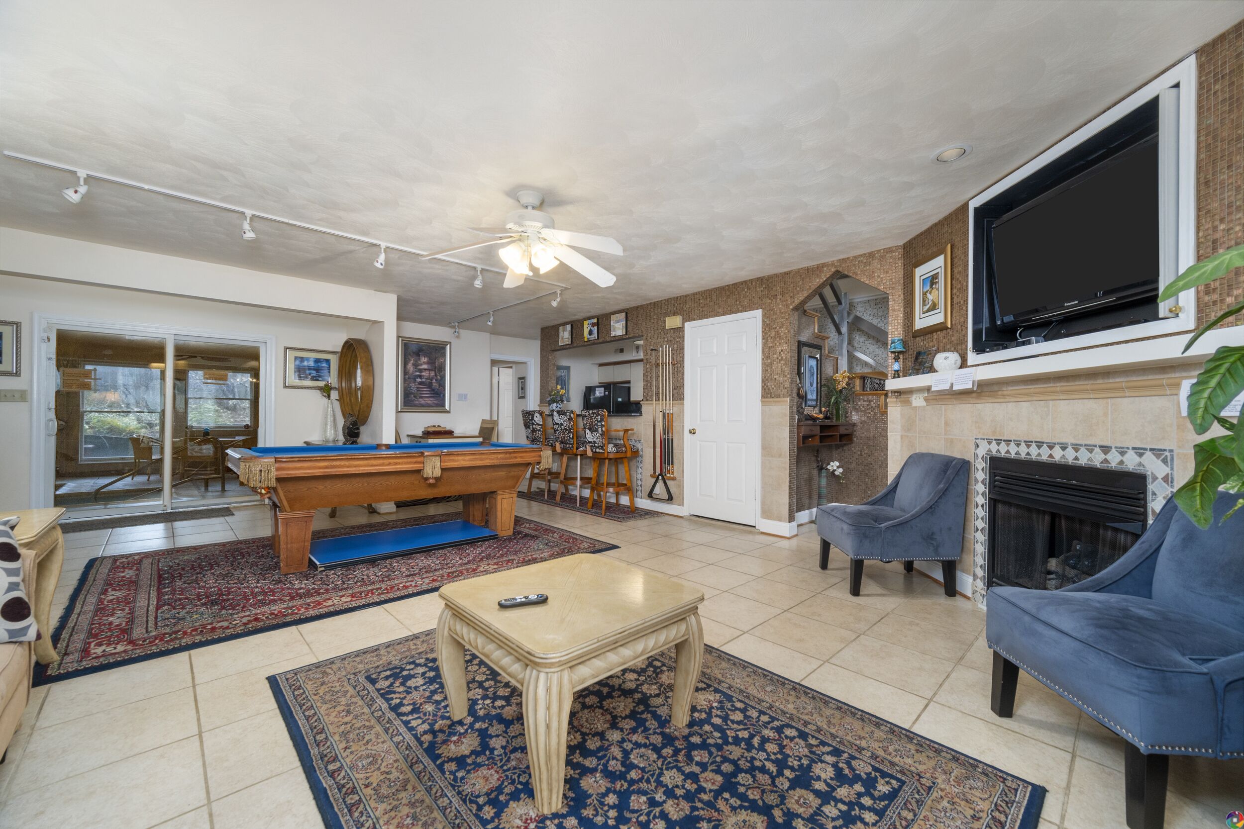 A living room with a pool table, a fireplace, and a TV mounted on the wall.