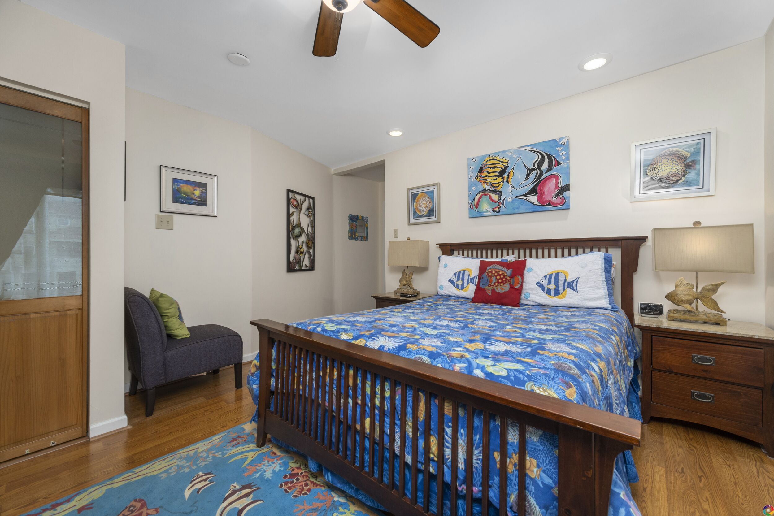 Un dormitorio con una cama de madera, una mesita de noche con lámparas, una silla y obras de arte en las paredes.