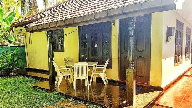 Una casa a un piano con tetto in tegole, un portico coperto con tavolo e sedie e un piccolo giardino.