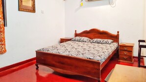 Una camera da letto con un letto di legno, un comodino, un tavolino e un condizionatore d'aria a parete, oltre a un quadro appeso al muro.
