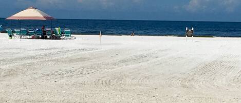 A beach with a row of beach chairs and a large umbrella.