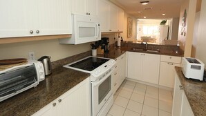 A kitchen with white cabinets, a microwave, a stove, a toaster, and a sink.