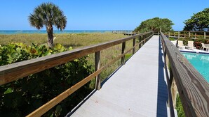 A wooden boardwalk leading to a pool area with a clear view of the ocean.