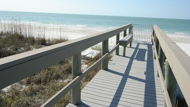 A wooden boardwalk leading to a beach with a bench and railing.