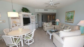 A living room with a white sofa, a dining table with chairs, a TV, and a ceiling fan.