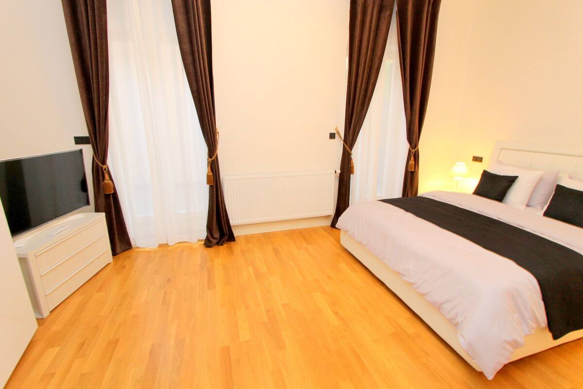 A bedroom with a bed, a TV, a dresser, and curtains.
