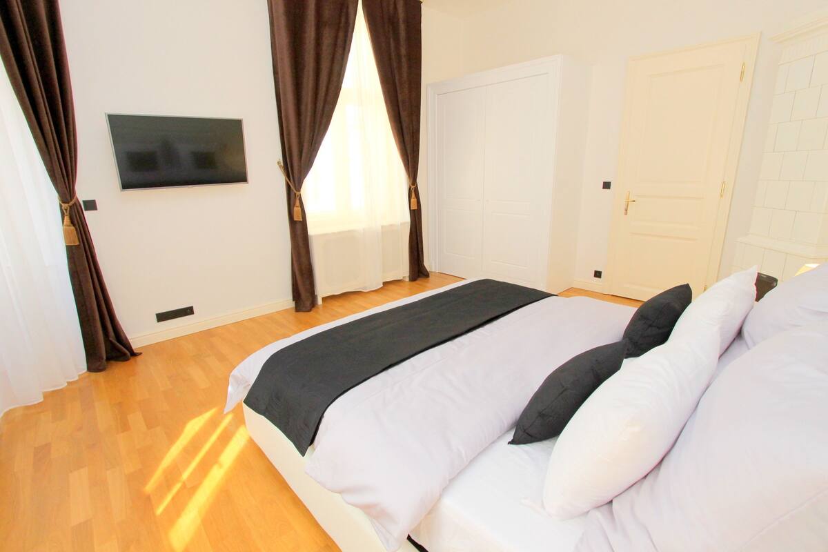 A bedroom with a bed, curtains, a television, and a door.