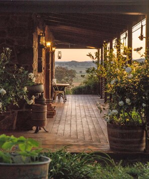 A rustic wooden deck with a table and chairs, surrounded by potted plants and a view of the countryside. - Stone Creek Cottage Farmstay (Mansfield)