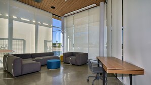Un espace de bureau moderne avec un grand canapé d’angle, un pouf bleu et une table en bois.