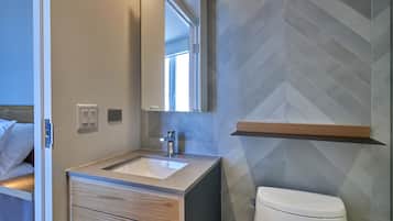 A modern bathroom with a wooden vanity, a large mirror, and a herringbone-patterned wall.