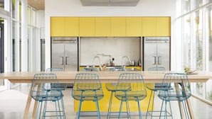 Une cuisine moderne avec des meubles de couleur jaune, des appareils en acier inoxydable et des chaises en fil de fer bleu.