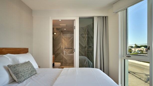 Une chambre d’hôtel avec un grand lit, une salle de bain avec douche et une vue sur la rue grâce à une grande fenêtre.
