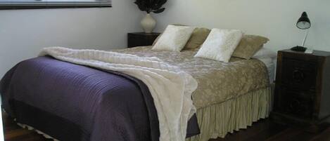 A bedroom with a bed, a nightstand, a lamp, and a potted plant.