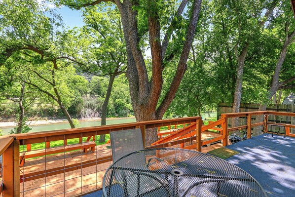 A deck with a table and chairs, overlooking a river and surrounded by trees.