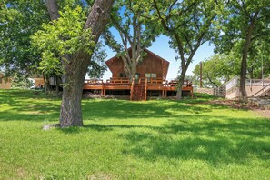 A wooden cabin with a deck and a ladder leading to a wooden staircase.