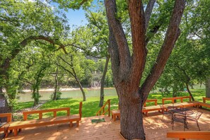Une terrasse en bois avec des bancs, donnant sur une étendue d’eau et entourée d’arbres.