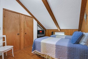 Een slaapkamer met een schuine kap, een houten garderobe, een bed met een sprei, een stoel en een televisie.