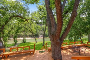 A wooden deck with benches and a table overlooking a river. - Perfect Spot on the Guadalupe River! Sleep up to 10 and Float all day! (New Braunfels)