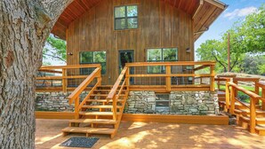 Une cabane en bois, avec des fondations en pierre, une terrasse en bois et un escalier menant à un balcon.