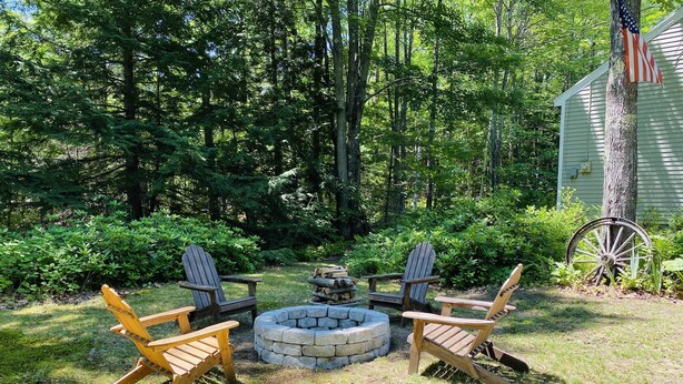 A backyard with a stone fire pit, wooden Adirondack chairs, and a wooden wheelbarrow. - Luxurious Farmhouse Style Home - Get away from it all in picturesque setting (Brownfield)