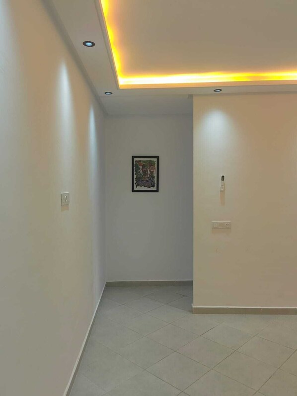 A hallway with a ceiling light, a framed picture on the wall, and a door on the right. - Tidy and Calm appartment  equiped with WiFI  close to airport and ocean (Tanger)