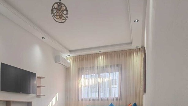 A living room with a green sofa, a flat-screen TV, a coffee table, and a window with curtains. - Tidy and Calm appartment  equiped with WiFI  close to airport and ocean (Tanger)