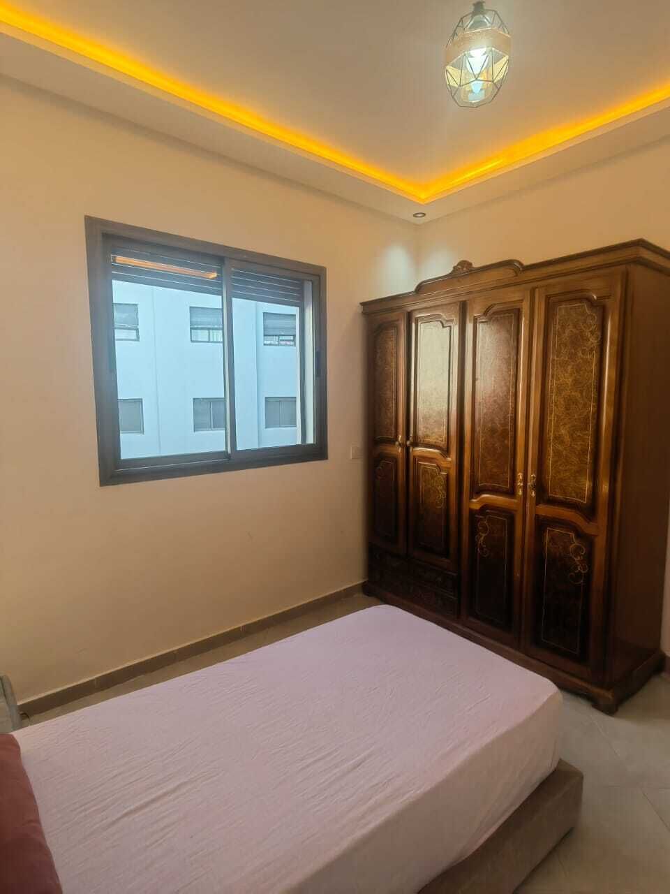 Ein Schlafzimmer mit Bett, Kleiderschrank, Fenster und Deckenleuchte.