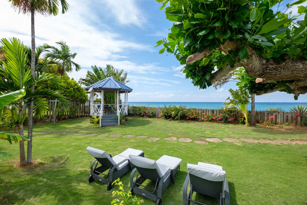A well-maintained garden with a gazebo, lounge chairs, and a view of the ocean.