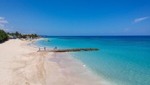Una playa con agua turquesa cristalina, una orilla de arena y un muelle de madera que se adentra en el mar.
