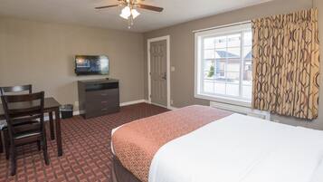 Quarto de hotel com cama, escrivaninha, cadeira, televisão e janela com cortinas.