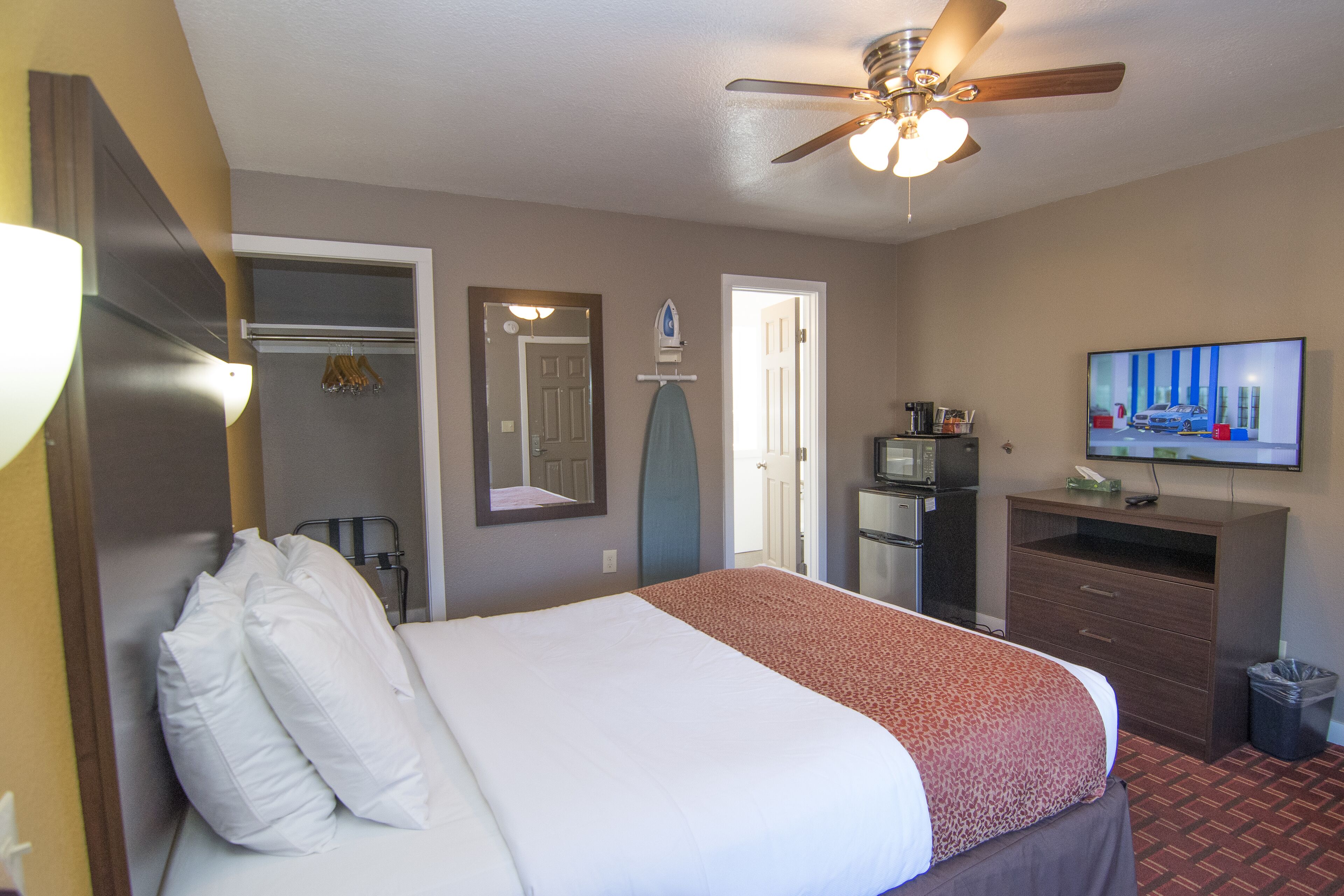 Habitación de hotel con cama, ventilador de techo, televisor, escritorio y cubo de basura.