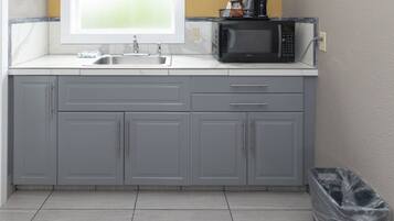 A small kitchen with grey cabinets, a stainless steel sink, and a black microwave.