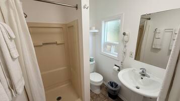 A bathroom with a shower, toilet, sink, and a window.