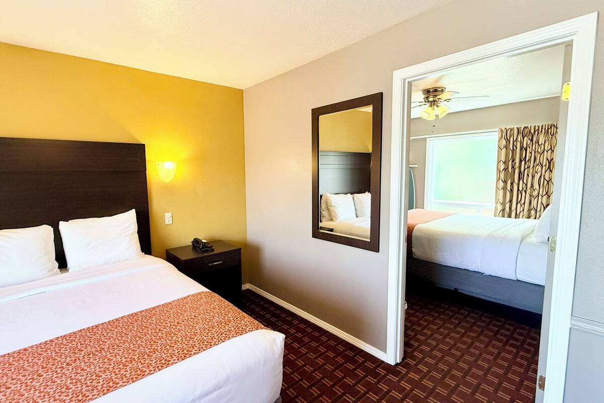 A hotel room with a large bed, bedside table, and a mirror reflecting another room.