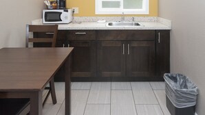 A compact kitchen with dark wooden cabinets, a white countertop, a microwave, and a sink. - Capitol Hill Motel (Portland)