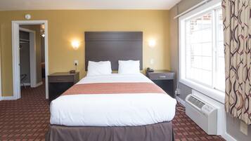 Una habitación de hotel con una cama grande, dos mesitas de noche, un calentador y una ventana con cortinas.