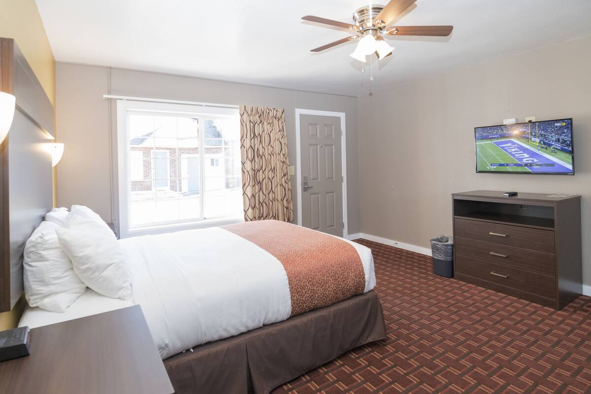 A hotel room with a bed, a desk, a television, and a ceiling fan.