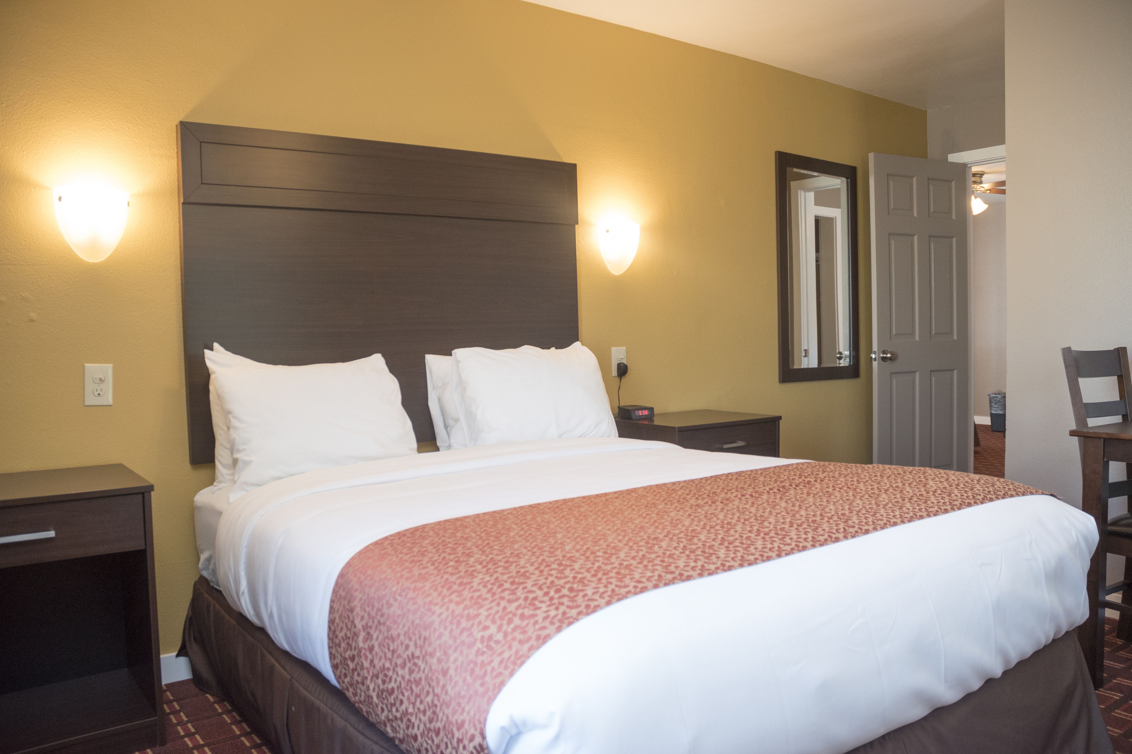 A hotel room with a large bed, two bedside tables, a nightstand, a chair, and a door.