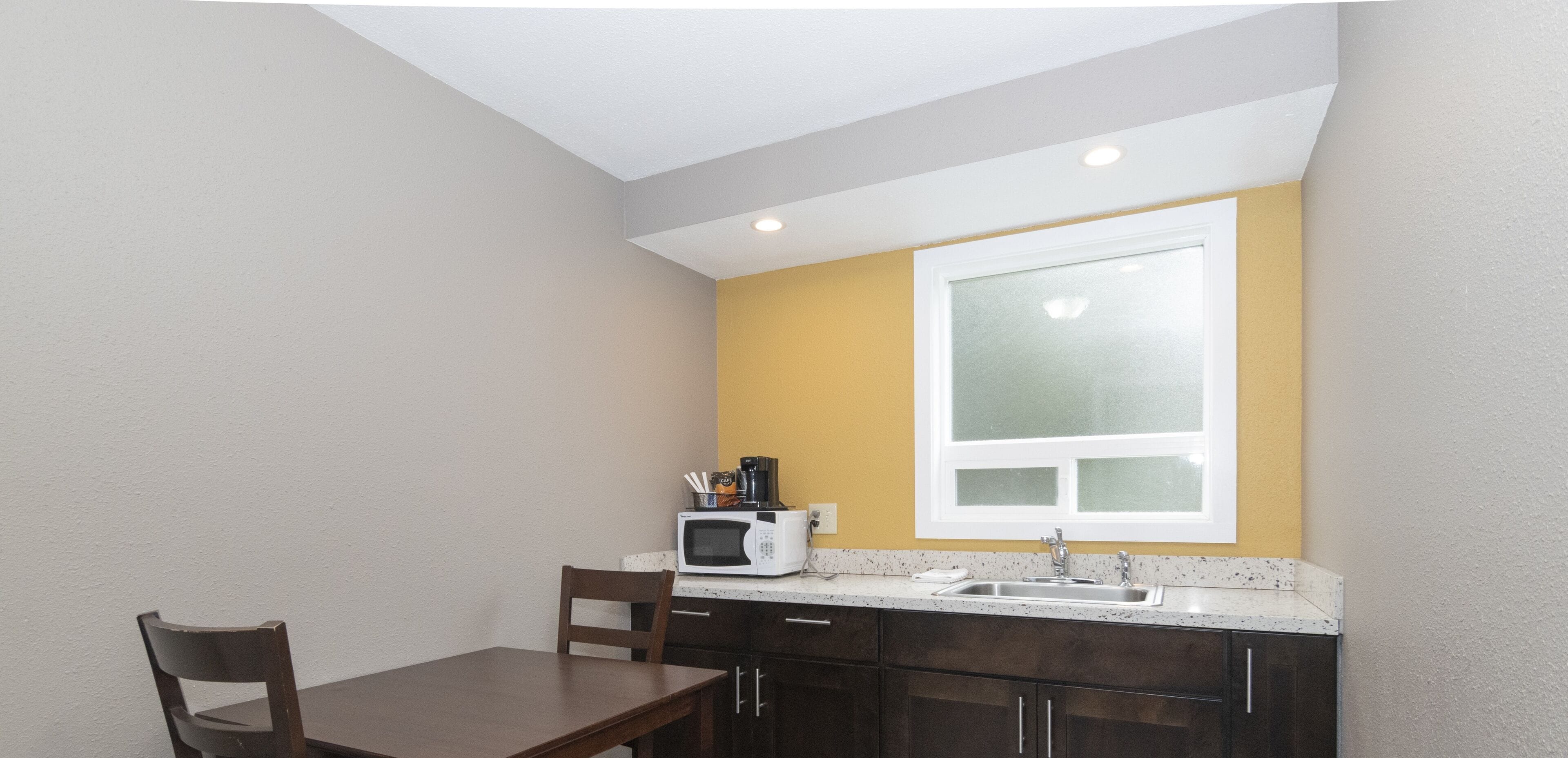 A compact kitchen with a microwave, sink, and a small dining area with a table and chair.