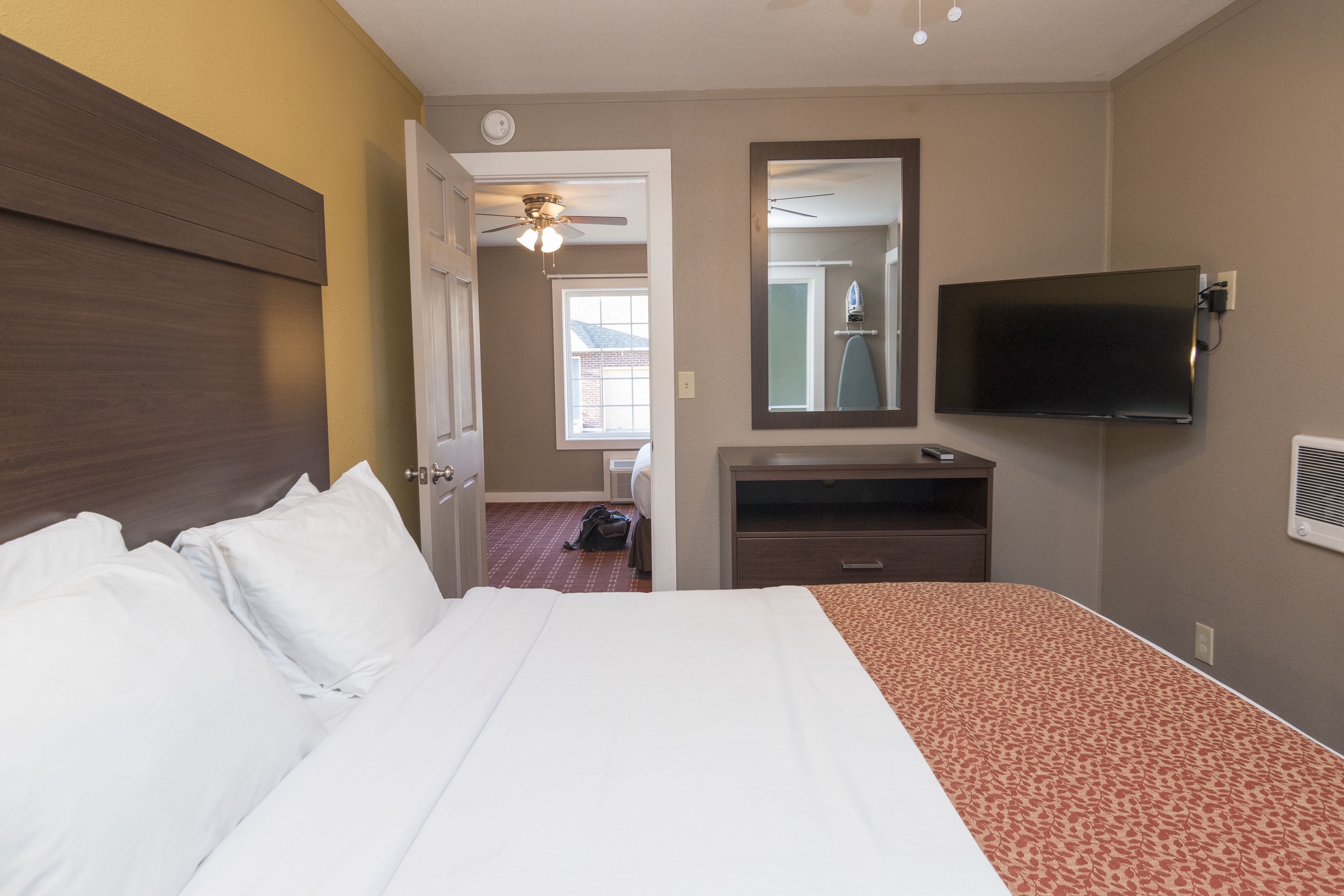 Ein Hotelzimmer mit einem großen Bett, einem flachbildfernseher an der Wand, einem Deckenventilator und einem Fenster mit Tageslicht.