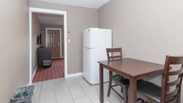 A small, clean room with a wooden dining table and chairs, a white refrigerator, and a trash bin.