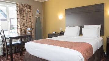 A hotel room with a large bed, a desk with a chair, a nightstand, and a window with curtains.