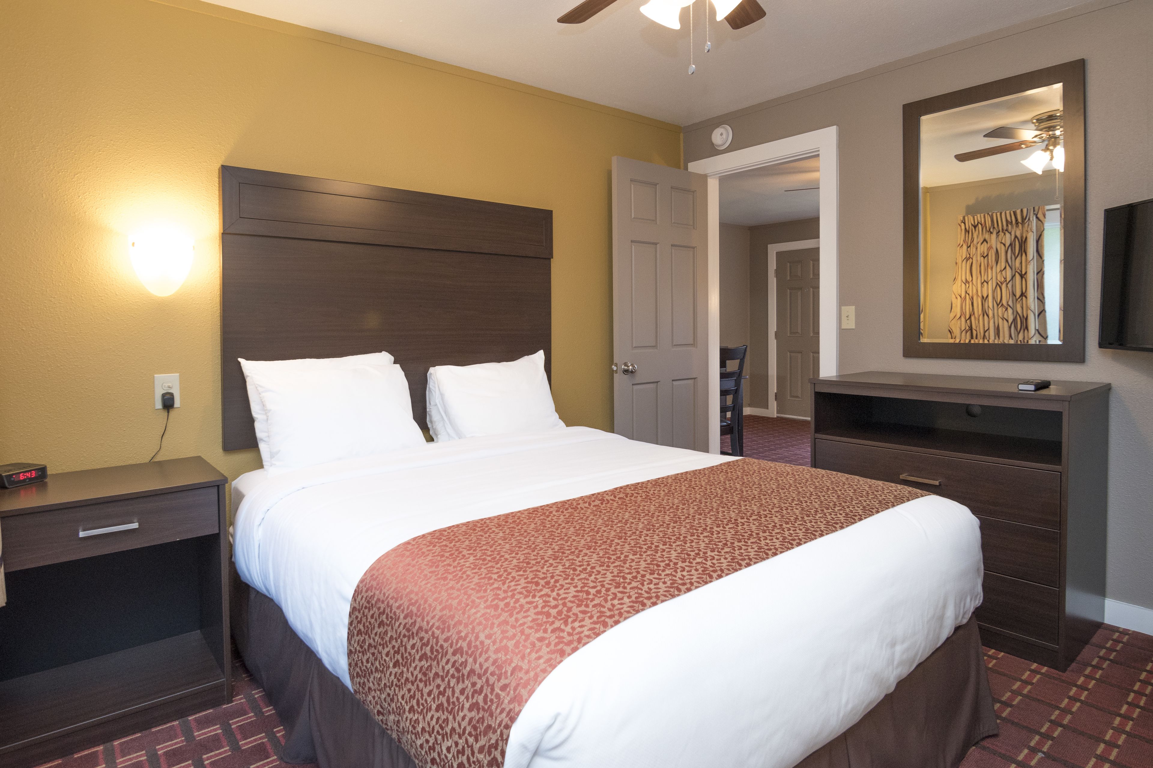 A hotel room with a large bed, a nightstand, a dresser, a mirror, and a ceiling fan.